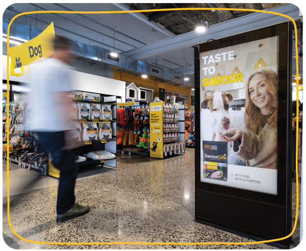 In‑store digital screen displaying pet food advertising at Petbarn Digital advertising screen inside a Petbarn store showing a pet food campaign, with shoppers walking past aisles of dog products.